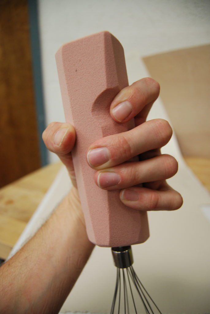 Hand holding pink foam model with whisk at one end